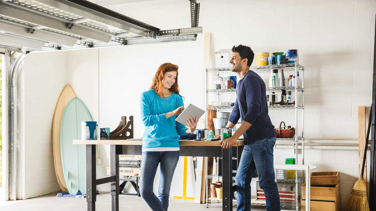 Happy man and woman talking while standing in a home garage and looking at a tablet.